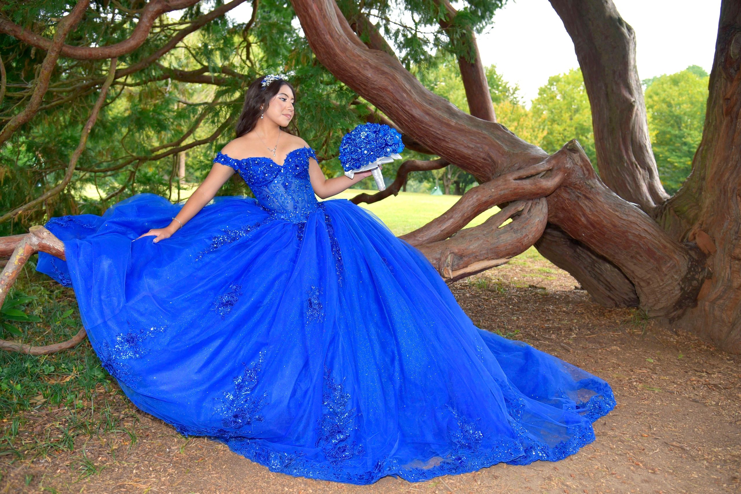 Woman in royal blue quinceañera ball gown under tree branches