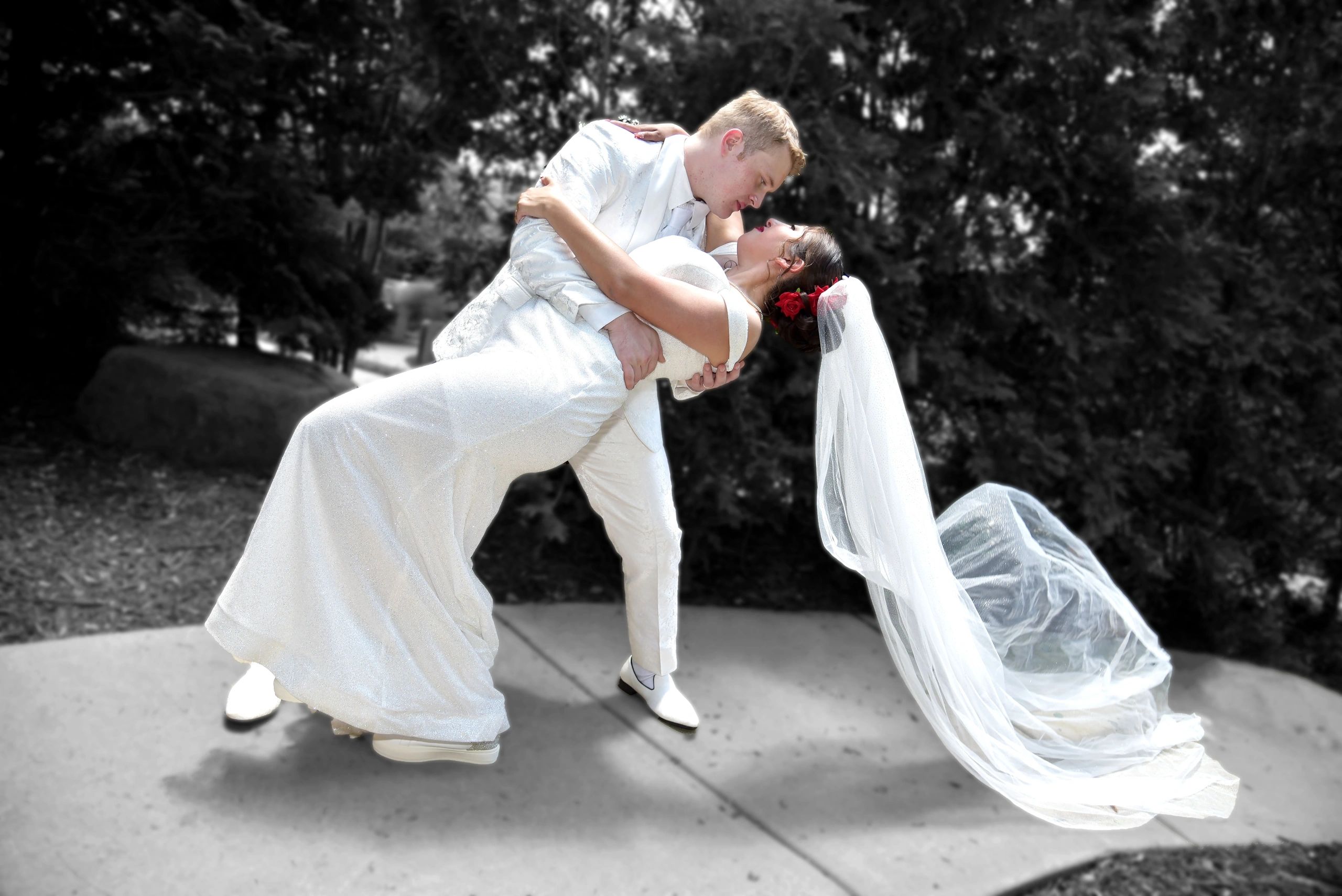 Groom dipping bride in white wedding dress with red bouquet